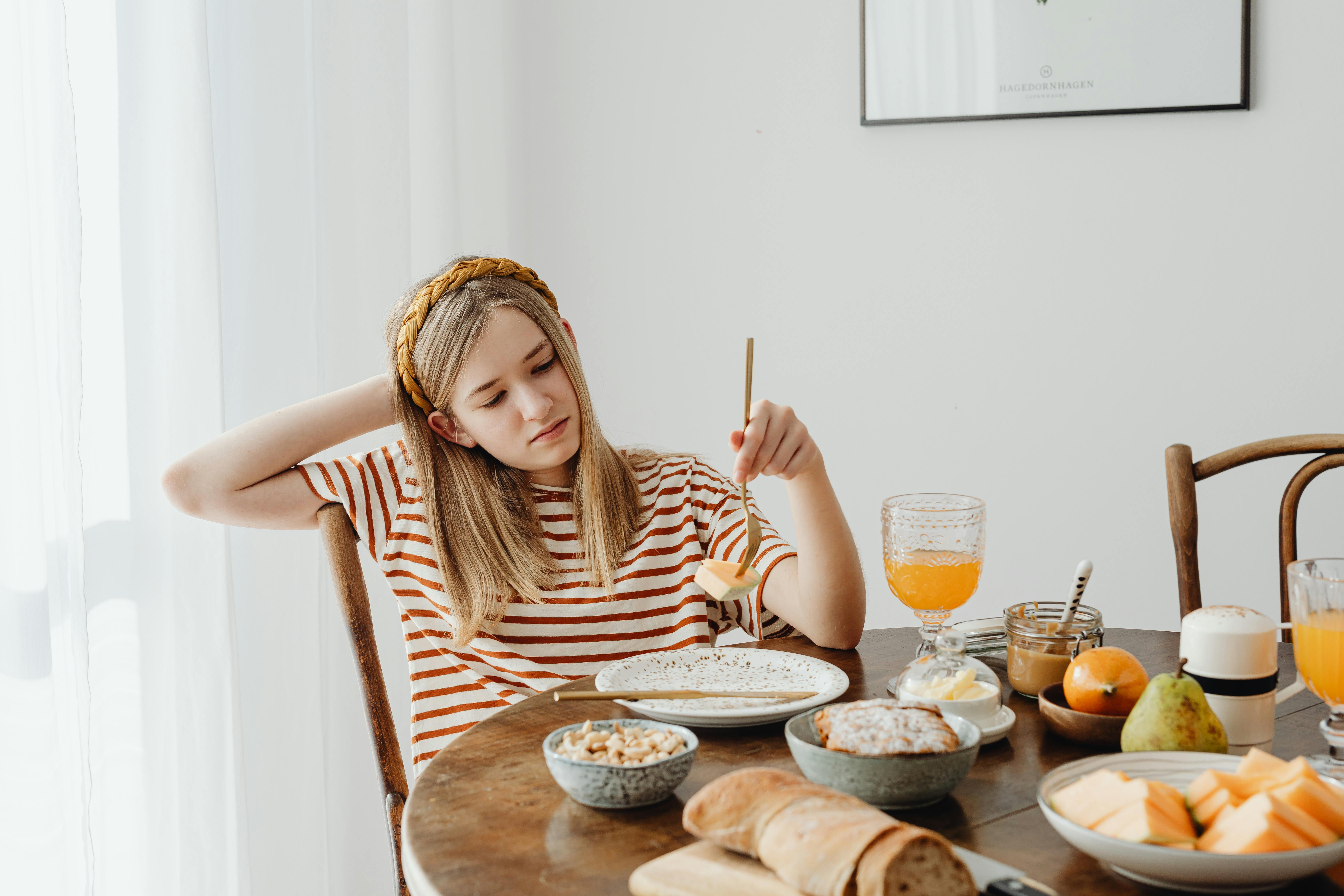 Junges Mädchen sitzt gedankenverloren am Frühstückstisch